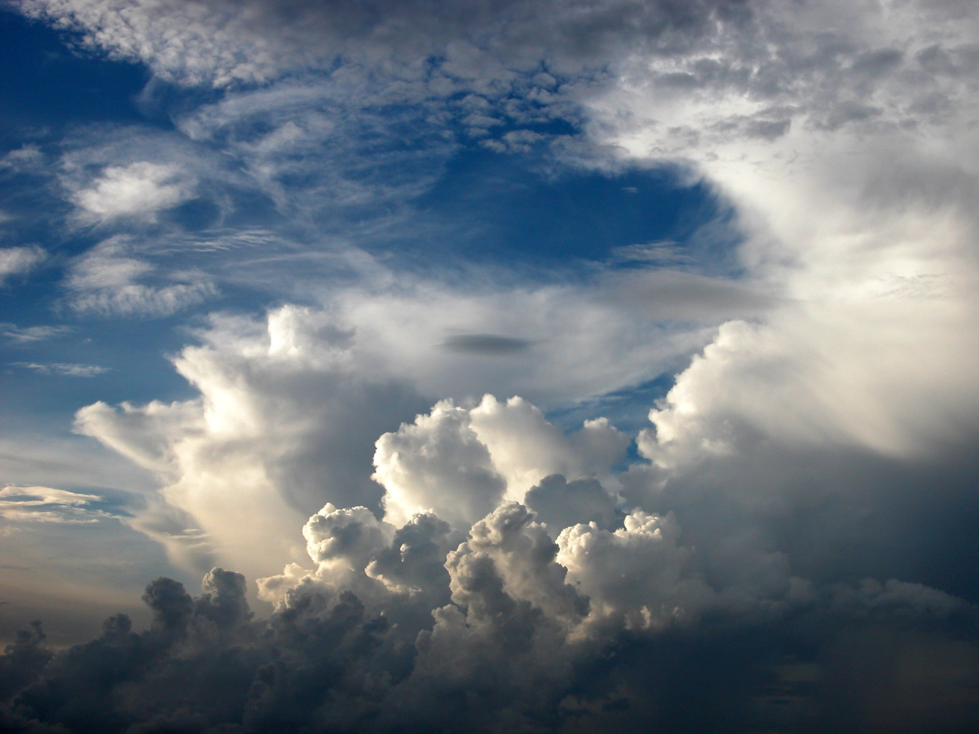 Dramatic towering white cumulonimbus clouds against a deep blue sky, with a clear opening revealing a small dark cloud